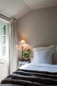 Französisches Bett mit Antiklampe auf dem Nachttischchen in elegantem Landhaus Schlafzimmer unterm Dach