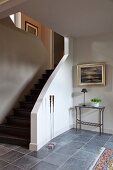 Grauer Fliesenboden in minimalistischem Vorraum und zierliche Konsole neben Treppenaufgang
