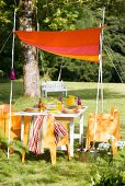 Brightly coloured, hand-sewn awning on white-painted bamboo canes above summery set table in garden