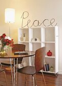 Modern dining area with wooden shell chairs in front of white shelves on castors; metal wire sign saying 'Peace' on top
