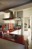 Modern L-shaped kitchen with red worksurfaces and protective grid around hob