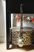 Aufbewahrungsbox im Leoparden-Look, darüber Schmuck auf Seil hängend