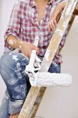 Renovating - woman sitting on ladder holding paintbrush and roller