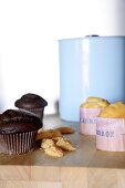 Chocolate muffins and pale pastries with Spanish-printed paper cases; light blue enamel pot in background
