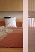 Double bed with pale bedspread against smooth wooden fronts of fitted cupboards; detail of sliding door with translucent bamboo blind