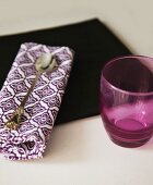 Purple drinking glass next to silver spoon on patterned linen napkin