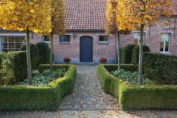 Garden with topiary trees and hedges in front of house with brick facade