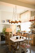 Wooden table and various wooden chairs below rustic pendant lamp in eclectic yet tasteful kitchen-dining room