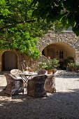 Gartentisch und Rattanstühle auf Kiesboden vor mediterranem Landhaus mit Rundbogen vor dem Eingang