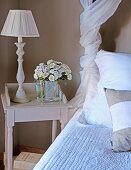 Table lamp and bouquet on rustic bedside table next to bed with scatter cushions