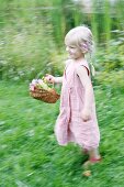 Blonde girl running through garden with basket of flowers