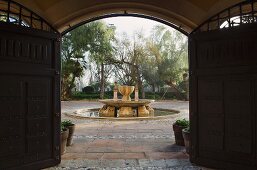 View of ornamental fountain in Mediterranean garden through open garden gate