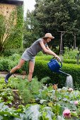 Frau giesst Pflanzen im Gemüsebeet