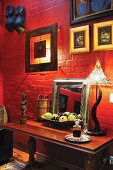Framed pictures above console table against brick wall painted red