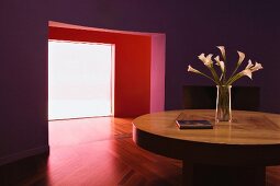 Runder Esstisch in lila getöntem Wohnraum mit Blick durch breiten Durchgang in rot getöntem Vorraum