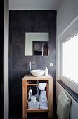 Wooden washstand with ceramic basin against grey-tiled wall in designer bathroom