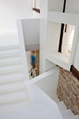 Verschachtelte, puristisch weiße Treppenanlage mit interessanten Durchblicken und Flächen mit Natursteinmauerwerk und Holzbalken. Person im Durchgang vermittelt einen Maßstab.