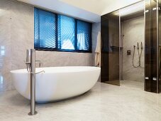 Freistehende Badewanne vor bodenebenem Duschbereich mit Glasschiebtüren im Marmor verkleidetem Bad