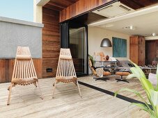Outdoor chairs made of wooden slats on terrace with stone floor and view into open-plan interior