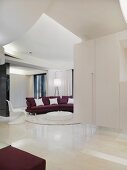 Offener weisser Wohnraum mit indirekter Deckenbeleuchtung und violettes Sofa um runden Bodentisch