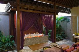 Badewanne mit violetten Vorhängen und Windlichtern in einem asiatischen Spa