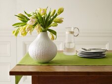 Blumenvase und Tellerstapel auf grünem Tischläufer