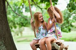 Smiling girls sitting in tree swing