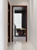 Blick von weiss glänzendem Gang durch die offene Badtür auf freistehende Designerwanne hinter einer Glaswand