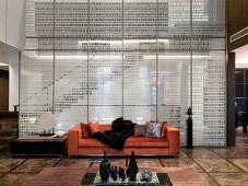 Bedruckte Glasscheibe vor Treppenaufgang und moderne Couch mit orangem Samtbezug in offenem Wohnraum