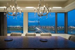 Kronleuchter über Esstisch mit Stühlen vor Fenster mit Blick auf Stadt in Abendstimmung
