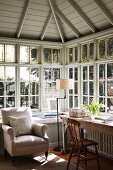 Bright home office in tasteful, country-house style with cushioned window seat in front of corner lattice glazing in window bay below wood-clad, hipped roof