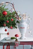 Christmas decorations hanging from branches in white, trophy-shaped china vase on table