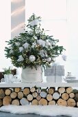 Christmas tree decorated with white baubles and presents on shelf resting on stacked logs