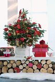 Geschmückter Weihnachtsbaum mit roten Kugeln und Geschenke auf weisser Ablage über geschichteten Holzscheiten