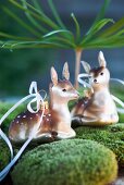 Two deer figurines on bed of moss gazing adoringly at one another