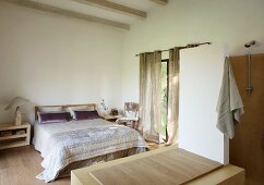 Blick von offenem Bad auf Doppelbett mit glänzender Tagesdecke in schlichtem Schlafzimmer