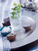 Sprig of peppermint in glass of water, sugar bowl and wooden printing blocks on metal dish