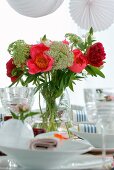 Summer bouquet in vase and white place settings with wine glasses on table