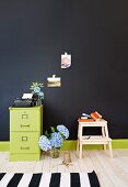 Bouquet of hydrangeas between green-painted office cabinet and step stool against black wall