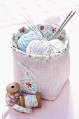 Balls of wool and knitting needles in pink basket next to vintage reels of yarn