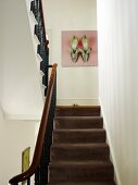 Blick über Treppe mit braunem Teppichbelag und schmiedeeisernem Geländer auf Bild mit Schuhmotiv an Wand in traditionellem Treppenhaus