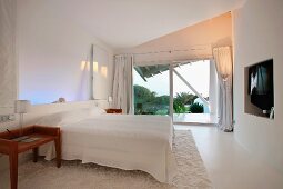 Weisses Schlafzimmer im Obergeschoss mit Blick auf Palmen durch die geöffnete Balkontür