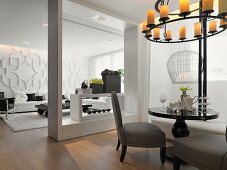 Schwarzer Bistrotisch unter Deckenkerzenleuchter in modernem Salon und Blick durch rahmenartige Öffnung ins Wohnzimmer