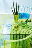 Ornaments in shades of aqua on glass table, wire chair with blue seat cushion & green plexiglass chairs