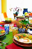 Farbenfroher Esstisch mit bunt bemaltem Keramikgeschirr und gemusterten Gläsern