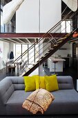 Hanging art object in front of a gray designer sofa with yellow pillows in a loft like living room