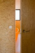 Open bathroom door made of OSB board and a view of a bath tub