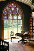 Detail of library in English stately home with view of summery parkland through large ecclesiastical window