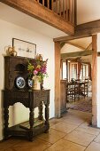 Ornaments on antique dresser in foyer of simple English country house with gallery, exposed beams and view into bright dining area