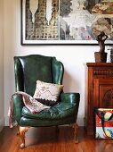 Wing-back armchair with green leather cover next to cabinet and contemporary artworks